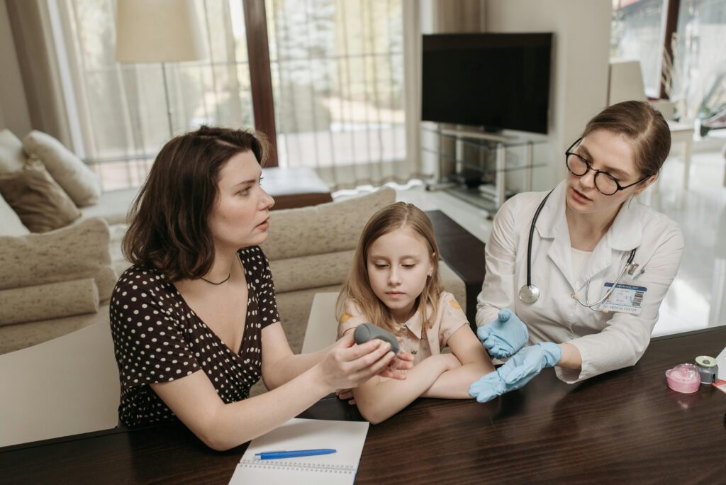 Doctor consults mother and daughter at home, discussing medical device in the living room.